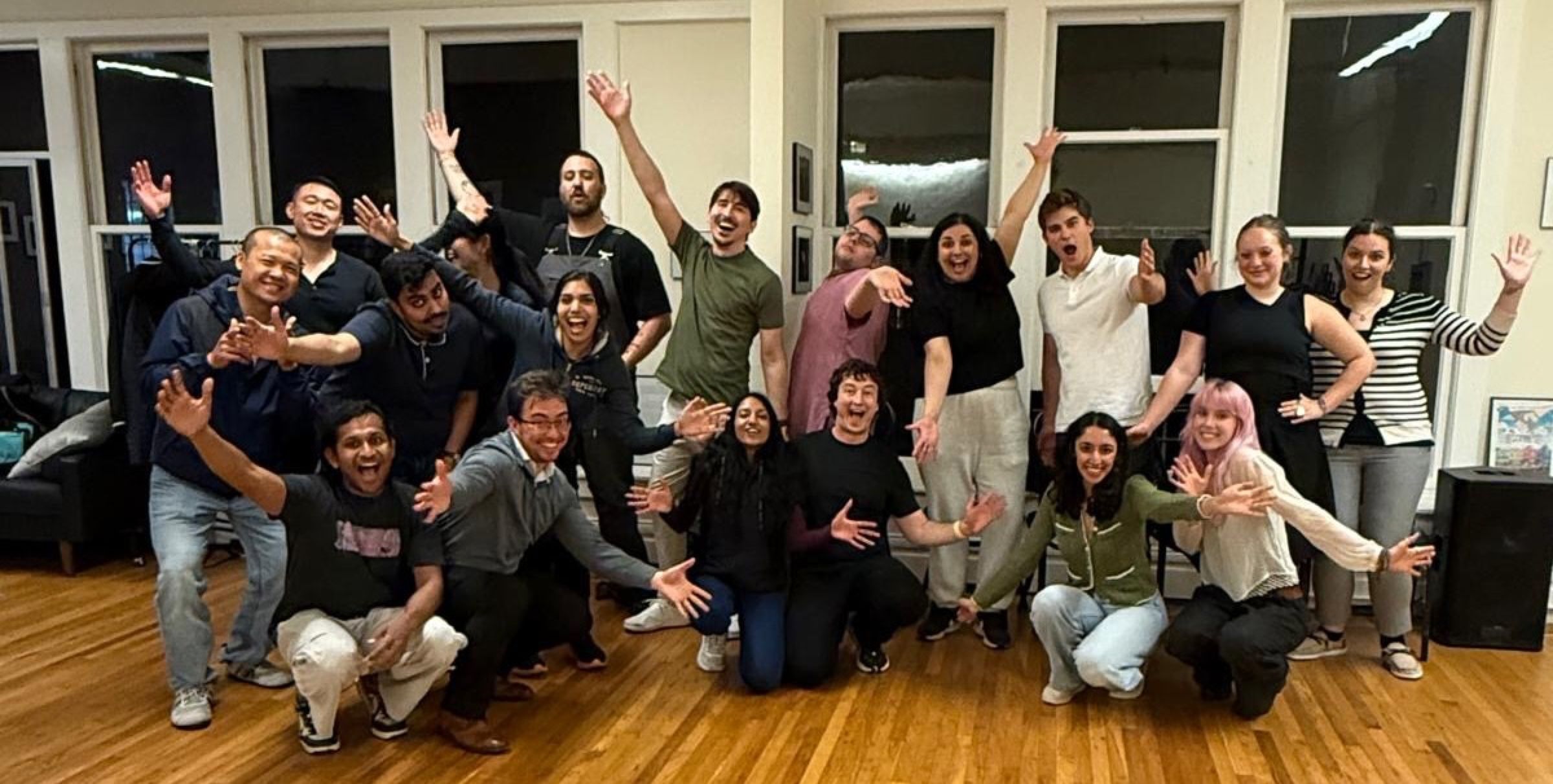 A group of about twenty people with arms up and big expressions, posing after an improv class.